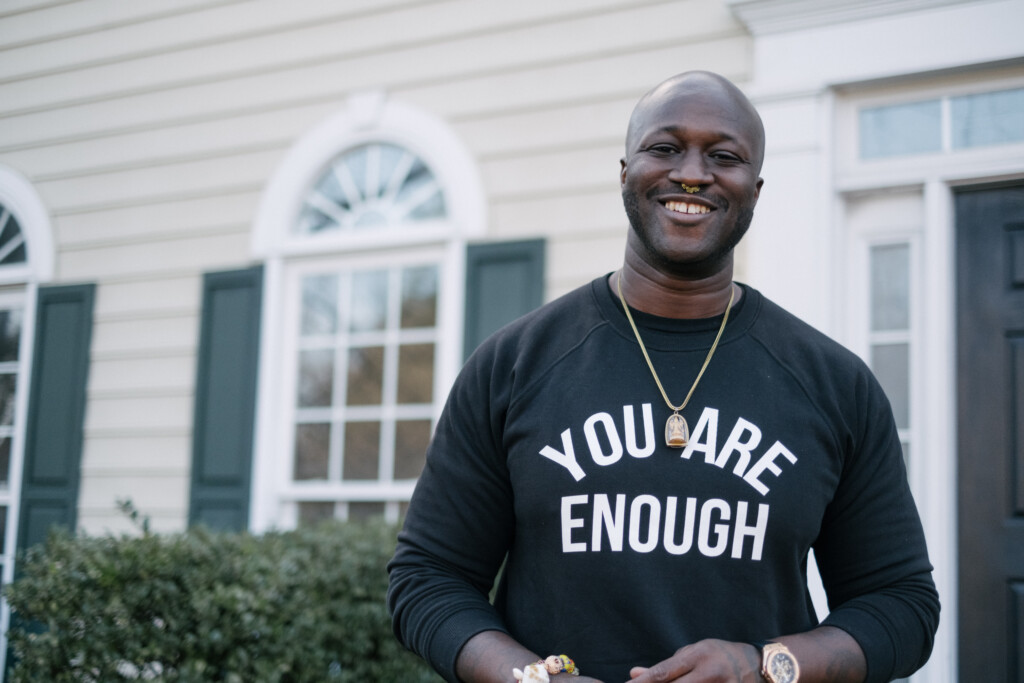 A smiling practitioner in a “You Are Enough” sweatshirt outside his home