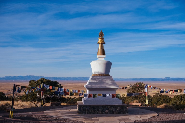 A white stupa with prayer flags above a wide valley under a blue sky